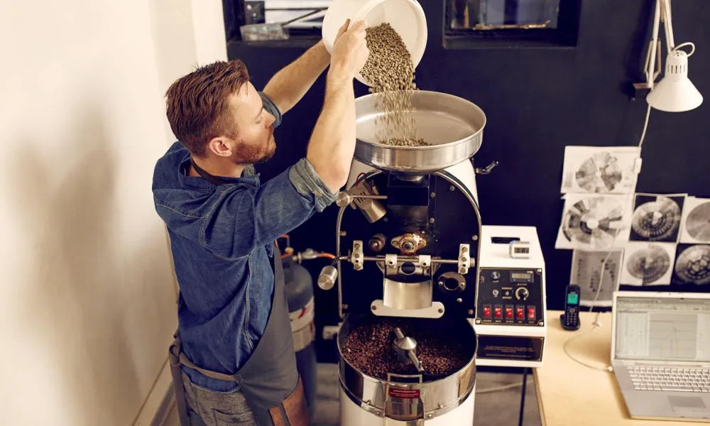 Man pouring coffee beans into a coffee roaster in a home kitchen setting.